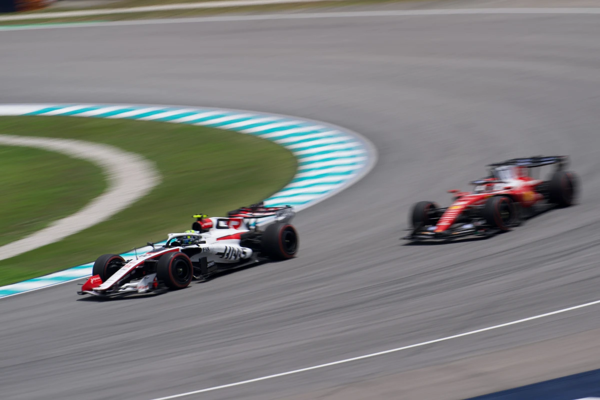 Haas followed by a blurred Ferrari through a sweeping corner at Sepang Circuit
