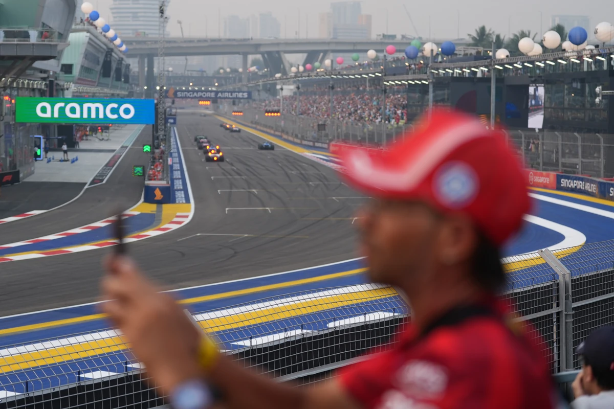Out-of-focus spectator in red holding a phone with the Singapore GP straight and grandstands behind