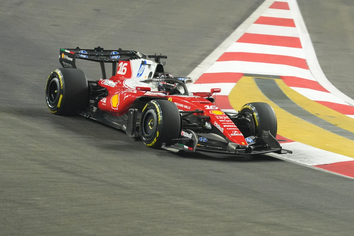 Ferrari number 16 cornering beside a red and white kerb at the Singapore GP at night