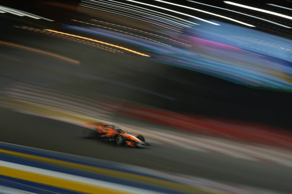 McLaren beneath diagonal light trails and a blurred trackside screen at the Singapore GP